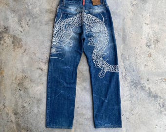 May include: Blue denim jeans with a white dragon design on the back. The jeans have a faded look and are distressed.