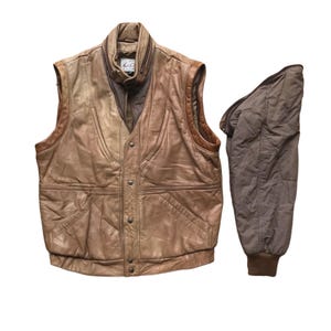 May include: A vintage brown leather vest with a high collar and a zip-up front. The vest has a button closure and two front pockets. A detachable brown sleeve is included. The vest is a light brown color with darker brown accents.