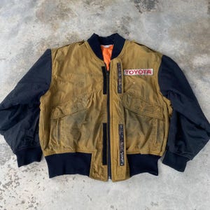 May include: A vintage brown and black bomber jacket with a zipper closure and a large "TOYOTA" patch on the right sleeve.