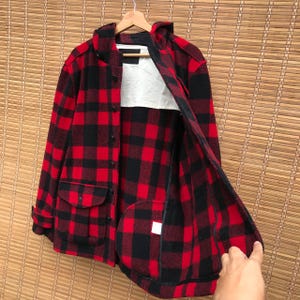 May include: Red and black plaid flannel jacket with a hood and a zipper closure. The jacket has two pockets on the front and a lined interior.