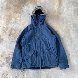 May include: A navy blue winter parka with a faux fur-lined hood. The jacket features a zipper closure, button details, and two front pockets. The parka is designed for cold weather and has a quilted lining for added warmth.