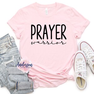 May include: Pink t-shirt with the text "PRAYER warrior" in black lettering.