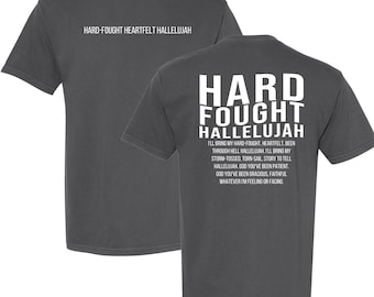 May include: A dark gray t-shirt with white text on the back that reads "Hard Fought Hallelujah" and a smaller text block that reads "I'll bring my hard-fought, heartfelt, been through hell Hallelujah, I'll bring my storm-tossed, torn-sail, story to tell Hallelujah, God you've been patient. God you've been gracious, faithful whatever I'm feeling or facing."