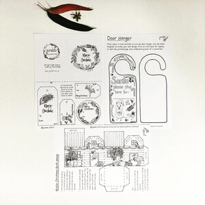 May include: A printable Christmas craft set featuring a door hanger, gift tags, and a 3D house. The door hanger says "Santa please stop here for:" and the house is decorated with Christmas bushes. The set is black and white and ready to be coloured.