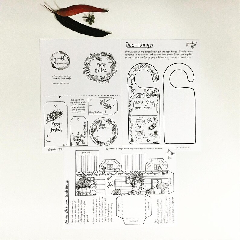 May include: A printable Christmas craft set featuring a door hanger, gift tags, and a 3D house. The door hanger says "Santa please stop here for:" and the house is decorated with Christmas bushes. The set is black and white and ready to be coloured.