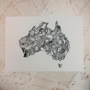 May include: A black and white illustration of the Australian continent filled with detailed drawings of animals, plants, and other elements. The artwork is on a white rectangular paper, with a detailed and intricate design.