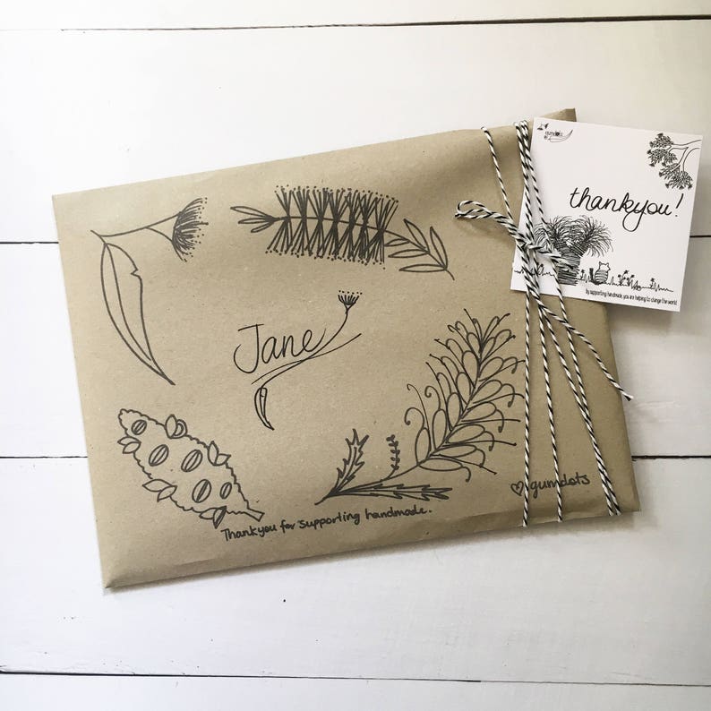 May include: A brown paper gift bag with a handwritten thank you note, a name, and a floral design. The bag is tied with twine and has the text "Thank you for supporting handmade."