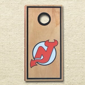 May include: A wooden cornhole board with a black border and a red and white New Jersey Devils logo.