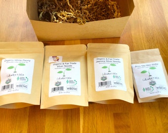 Könnte beinhalten: Vier braune Papiertüten mit weißen Etiketten, die verschiedene Teesorten enthalten. Die Etiketten tragen den Text "Cultivate Tarte" und "WBENC". Die Teesorten sind Organic White Peony, Organic & Fair Trade Silver Needle, Organic & Fair Trade Jasmine Silver Needle und Shou Mei Mini Wafer.
