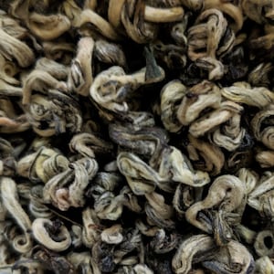 May include: Close-up of loose leaf green tea, with a light brown and white color, twisted into small, curled shapes.