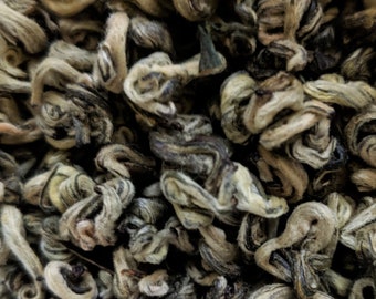 May include: Close-up of loose leaf green tea, with a light brown and white colour, twisted into small, curled shapes.