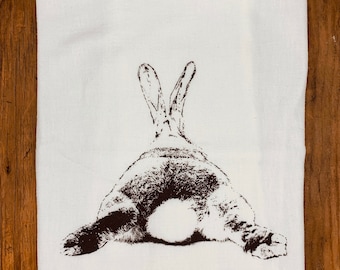 May include: A white kitchen towel with a brown silhouette of a rabbit's rear end printed on it.