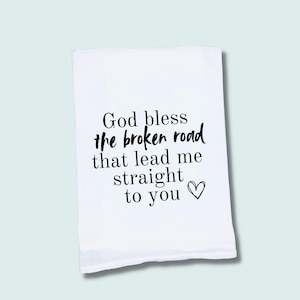 May include: White kitchen towel with black text that reads "God bless the broken road that lead me straight to you" with a small heart symbol.