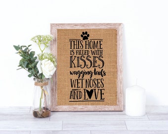 May include: A burlap sign with a wooden frame, featuring the text "This home is filled with kisses, wagging tails, wet noses and love" with a paw print and heart graphic.
