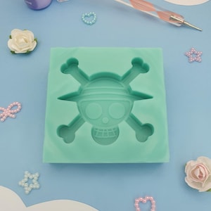 Peut inclure: Un moule en silicone vert en forme de crâne et d'os croisés. Le crâne porte un chapeau de paille et a un sourire narquois.