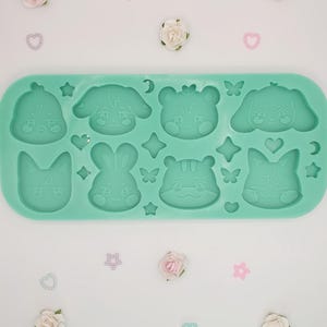 Può includere: Uno stampo in silicone verde chiaro con otto facce di animali dei cartoni animati, tra cui un uccello, un cane, un orso, un gatto, un coniglio e una tigre. Lo stampo è circondato da stelle, cuori e farfalle decorative. Piccoli fiori rosa e bianchi e abbellimenti a forma di cuore sono sparsi.