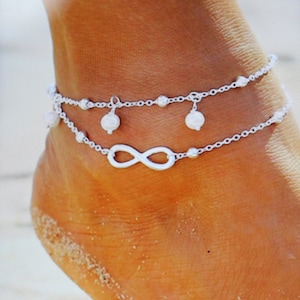 Peut inclure: Bracelet de cheville argenté avec un charme en forme d'infini et de petits accents de perles.