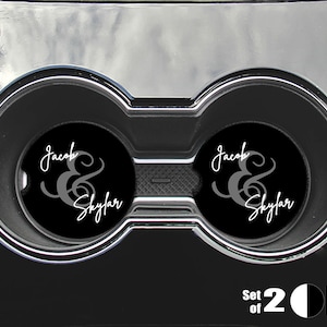 May include: Set of two black car coasters with white text that reads "Jacob & Skyler" in a cursive font. The coasters are in a car cup holder.