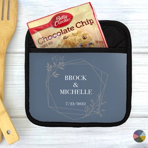 May include: A blue pot holder with a geometric design and floral accents. The text "Brock & Michelle 7/22/2022" is printed on the pot holder.