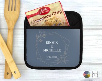May include: A blue pot holder with a geometric design and floral accents. The text "Brock & Michelle 7/22/2022" is printed on the pot holder.