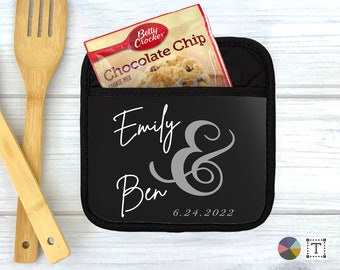 May include: Black pot holder with a pocket for a small item. The pot holder has the names "Emily & Ben" and the date "6.24.2022" printed on it in white.
