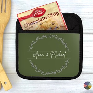 May include: Green pot holder with a black border and a wreath design with the text "Anna & Michael".