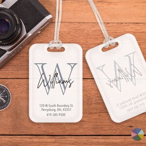 May include: White luggage tag with a gray letter W and the name Williams written in cursive. The tag also includes an address and phone number: 120 W South Boundary St. Perrysburg, OH, 43551, 419-385-9500.