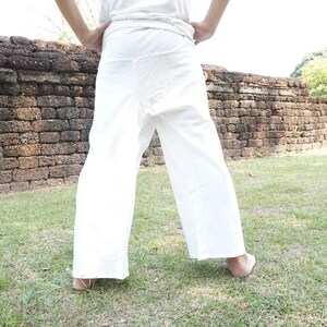 May include: White wrap pants with a wide leg design. The pants are made of a lightweight fabric and are worn outdoors. The person is standing on grass in front of a brick wall.
