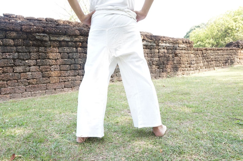 May include: White wrap pants with a wide leg design. The pants are made of a lightweight fabric and are worn outdoors. The person is standing on grass in front of a brick wall.