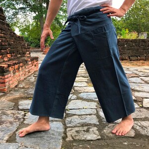 Pode incluir: Cal&ccedil;as envolventes azul escuro com cintura com cord&atilde;o e dois bolsos frontais. As cal&ccedil;as de perna larga s&atilde;o feitas de um tecido macio e s&atilde;o adequadas para roupas casuais. As cal&ccedil;as s&atilde;o mostradas ao ar livre em um caminho de pedra.