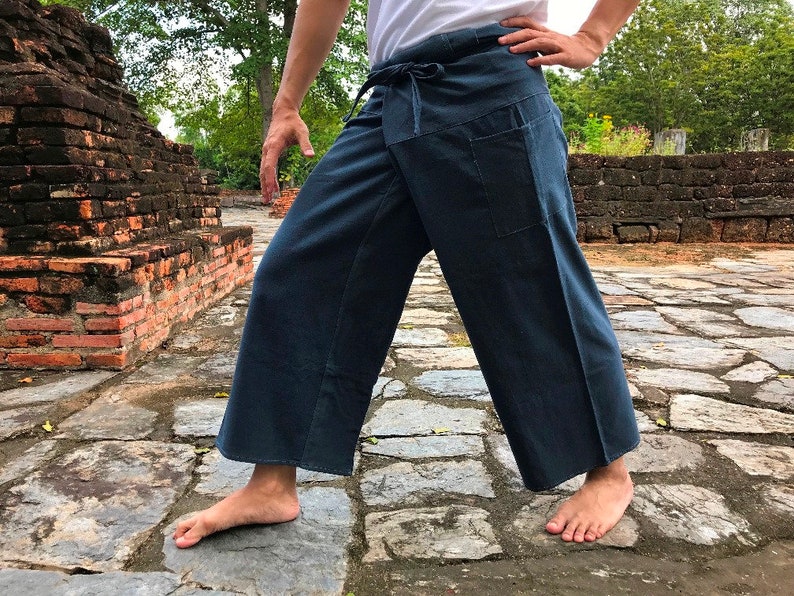 Pode incluir: Cal&ccedil;as envolventes azul escuro com cintura com cord&atilde;o e dois bolsos frontais. As cal&ccedil;as de perna larga s&atilde;o feitas de um tecido macio e s&atilde;o adequadas para roupas casuais. As cal&ccedil;as s&atilde;o mostradas ao ar livre em um caminho de pedra.