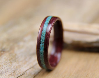 May include: A wooden ring with a thin turquoise inlay. The ring is dark red and has a smooth, polished finish.