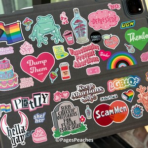 a variety of stickers on a laptop, including a rainbow flag, a frog, a mushroom, and other colorful and diverse stickers.
