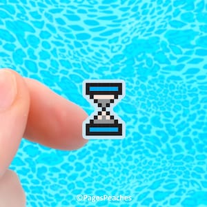 May include: A pixelated hourglass sticker with a black outline, blue top and bottom bars, and a white center. The sticker is held between two fingers against a blue patterned background. The sticker is small and detailed.