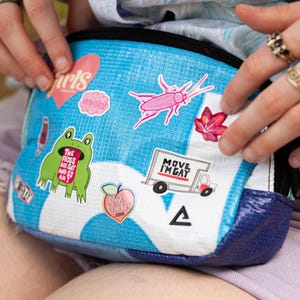 A person's hands holding a colorful, patterned bag with various stickers and designs on it.