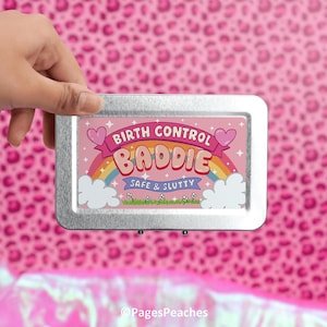 May include: A silver metal container with a pink graphic. The graphic features the text "BIRTH CONTROL BADIE" above a rainbow, with "SAFE & SLUTTY" below. The background is a pink leopard print pattern.