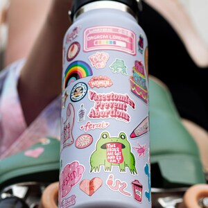 A colorful water bottle with various stickers and designs on it, including a frog, a rainbow, and other whimsical elements.
