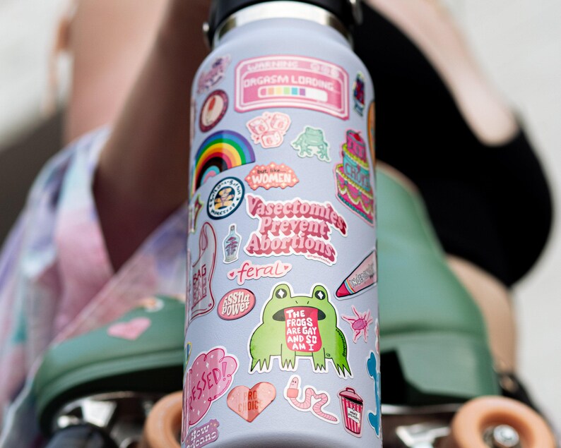 A colorful water bottle with various stickers and designs on it, including a frog, a rainbow, and other whimsical elements.