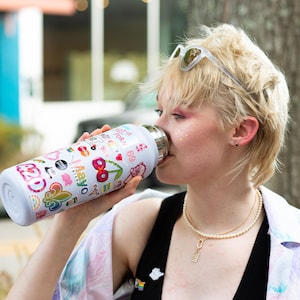 A woman with short blonde hair is drinking from a colorful water bottle with various stickers on it.