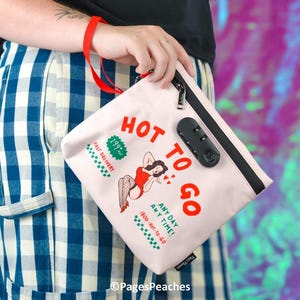 May include: A light pink zippered pouch featuring a black combination lock and red text that reads HOT TO GO. The graphic includes a person in a red bodysuit, green text stating 199 HOT, FAST DELIVERY, ANY DAY ANY TIME, and 1800-HOT-TO-GO.