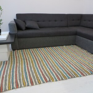 Puede incluir: Una alfombra rayada con una variedad de colores, incluyendo amarillo, azul, gris y rojo, en un sal&oacute;n con un sof&aacute; de esquina gris.