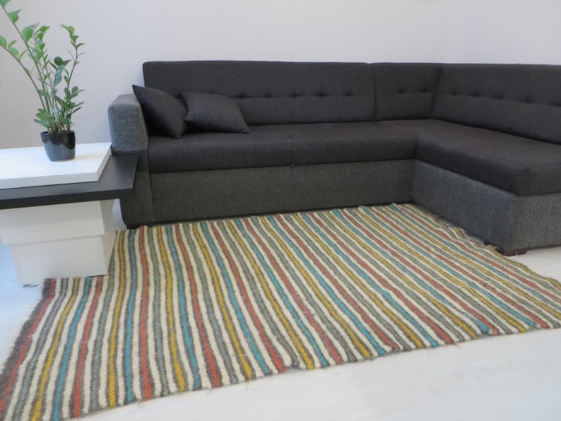 Puede incluir: Una alfombra rayada con una variedad de colores, incluyendo amarillo, azul, gris y rojo, en un sal&oacute;n con un sof&aacute; de esquina gris.