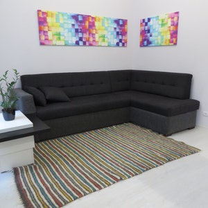 Puede incluir: Un sof&aacute; seccional negro con una alfombra rayada delante. Dos pinturas abstractas coloridas cuelgan en la pared detr&aacute;s del sof&aacute;.