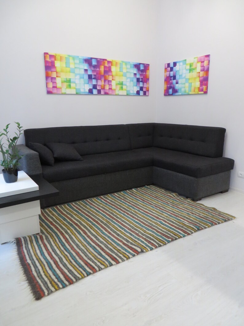 Puede incluir: Un sof&aacute; seccional negro con una alfombra rayada delante. Dos pinturas abstractas coloridas cuelgan en la pared detr&aacute;s del sof&aacute;.