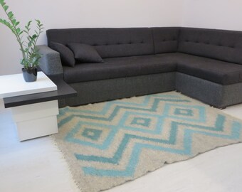 May include: A light blue and white patterned rug with a geometric design. The rug is placed in front of a grey sectional sofa.