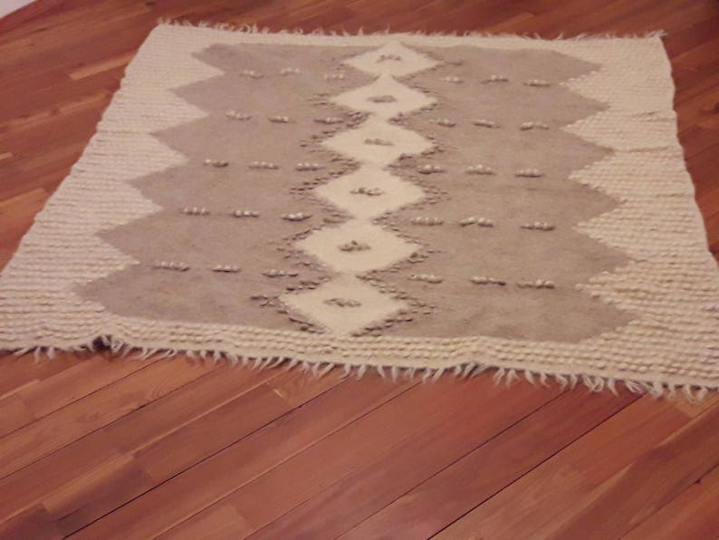 May include: A white and gray woven rug with a geometric pattern. The rug has a fringe border.