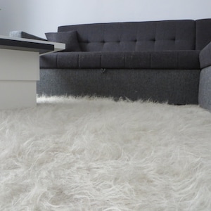 May include: A white fluffy rug in front of a gray sectional sofa.