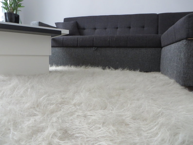May include: A white fluffy rug in front of a gray sectional sofa.