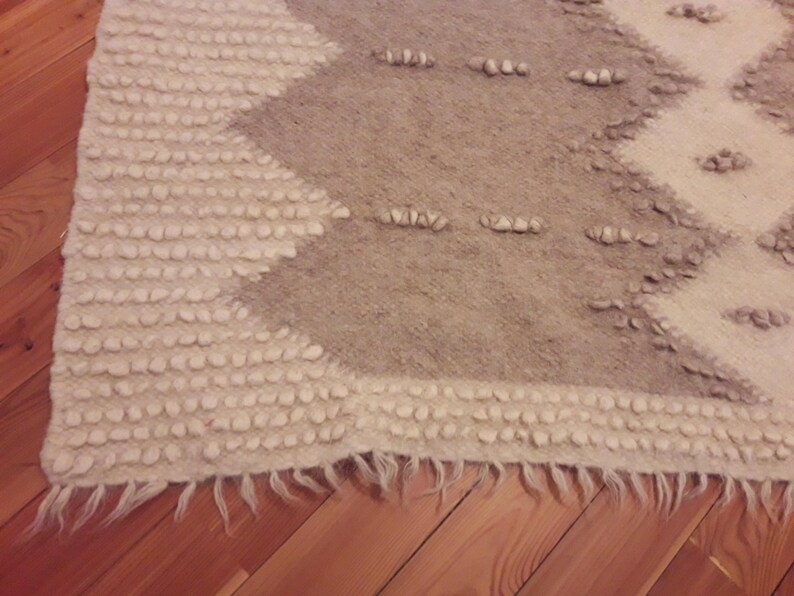 May include: A white and gray woven rug with a geometric pattern. The rug has a fringe border and is made of a soft, textured material.