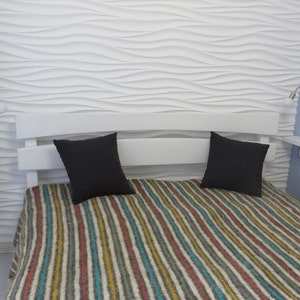 Puede incluir: Una estructura de cama blanca con una cabecera con un patr&oacute;n de ondas. La cama tiene una manta a rayas y dos almohadas negras. Hay dos apliques de pared con bombillas a cada lado de la cama.